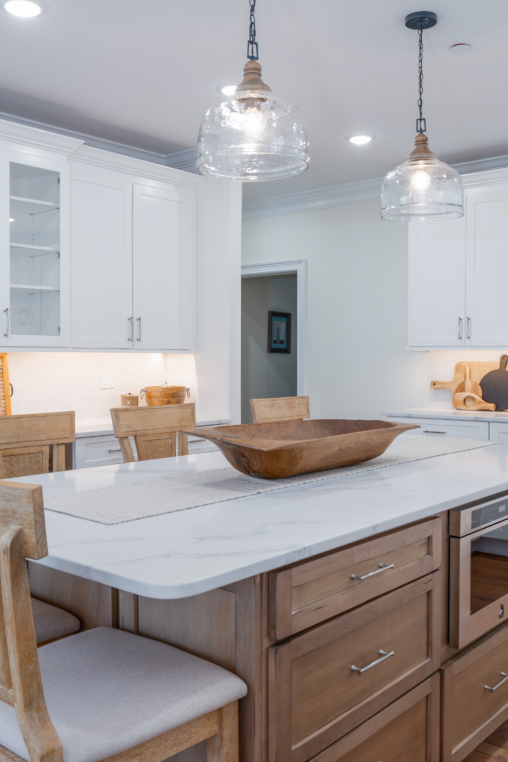 A modern white kitchen, with a wooden center island, and overhead lamp fixtures.