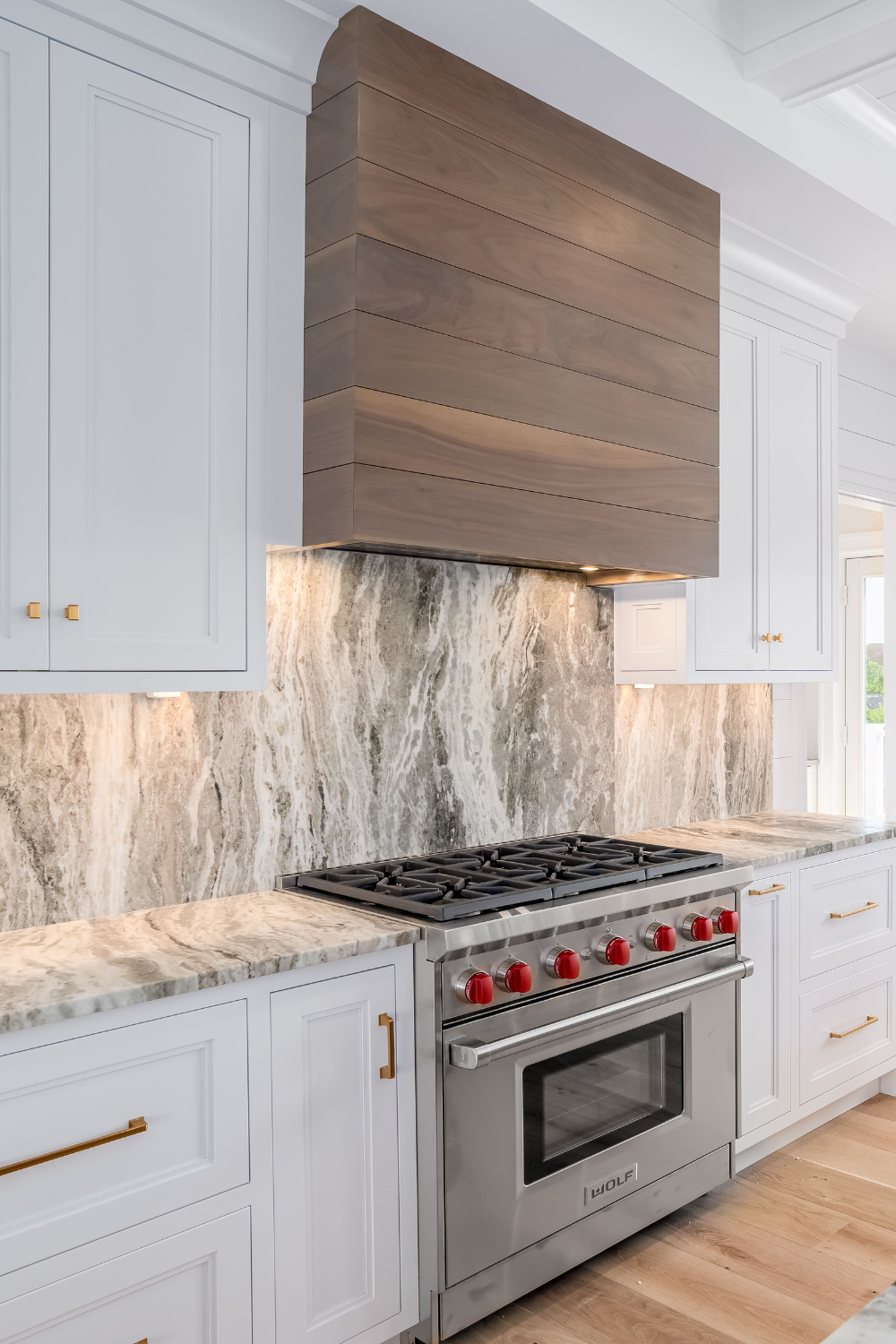 White kitchen cabinets, wooden oven range hood, marble backsplash.