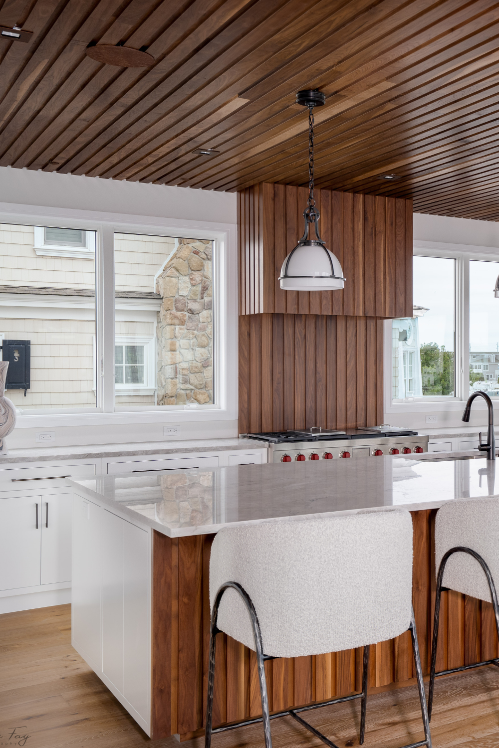 A modern kitchen with wooden ceiling, white cabinets, and white island with wooden accents.