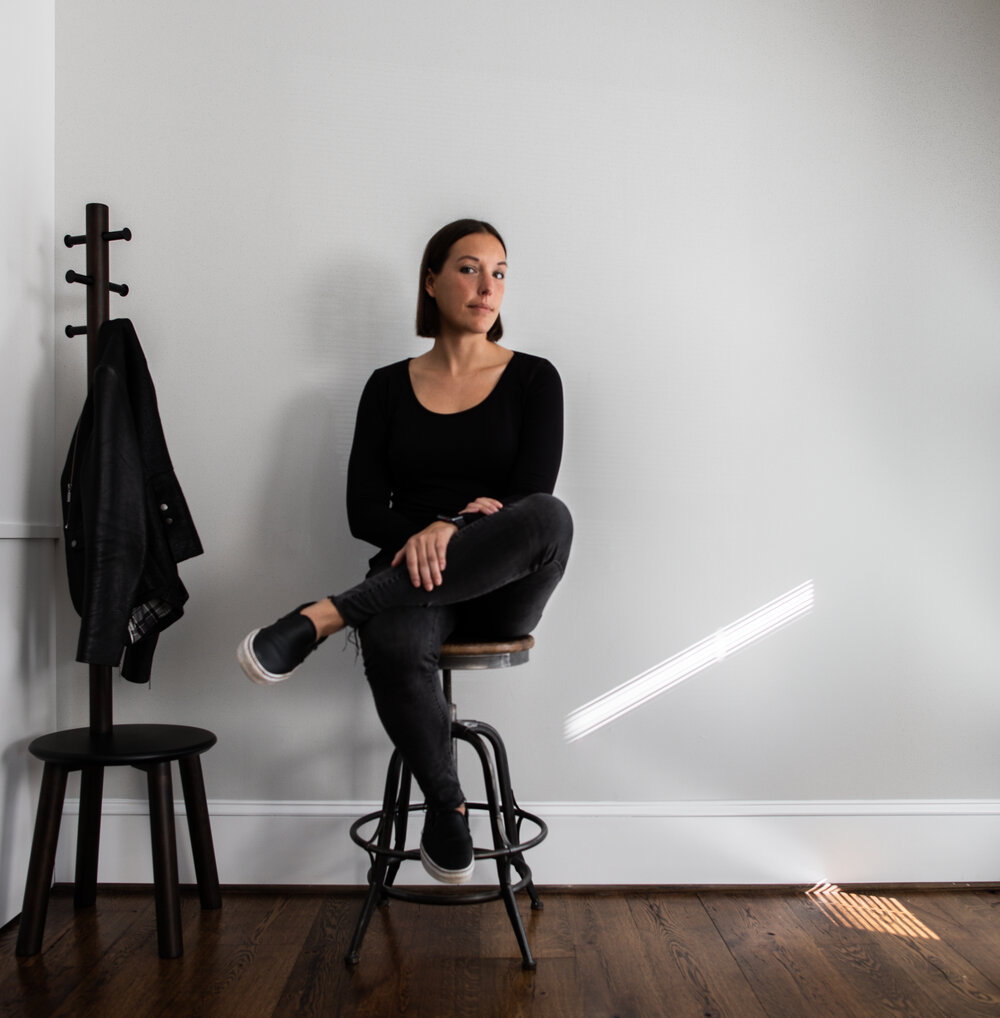 A woman sitting on a chair next to a coat rack.