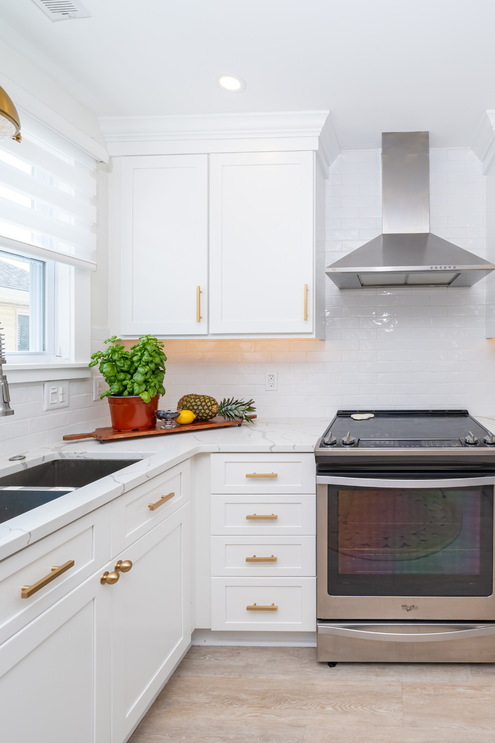 A kitchen with white cabinets, gold hardware, a stainless steel oven and range, and wooden floors. 