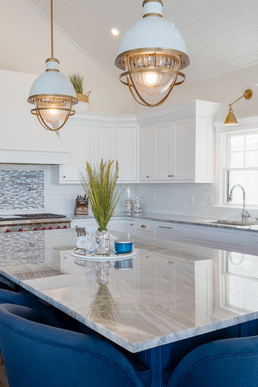 A kitchen with white cabinets, a marble center island, blue chairs, and gold hardware and accents.