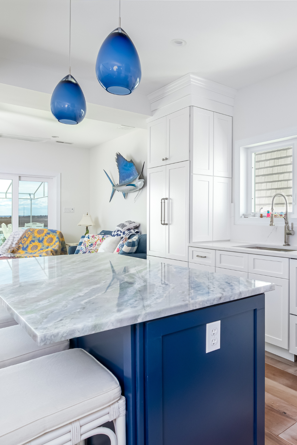 Kitchen with white cabinets, blue lamp fixtures, overlooking a beach-themed living room.