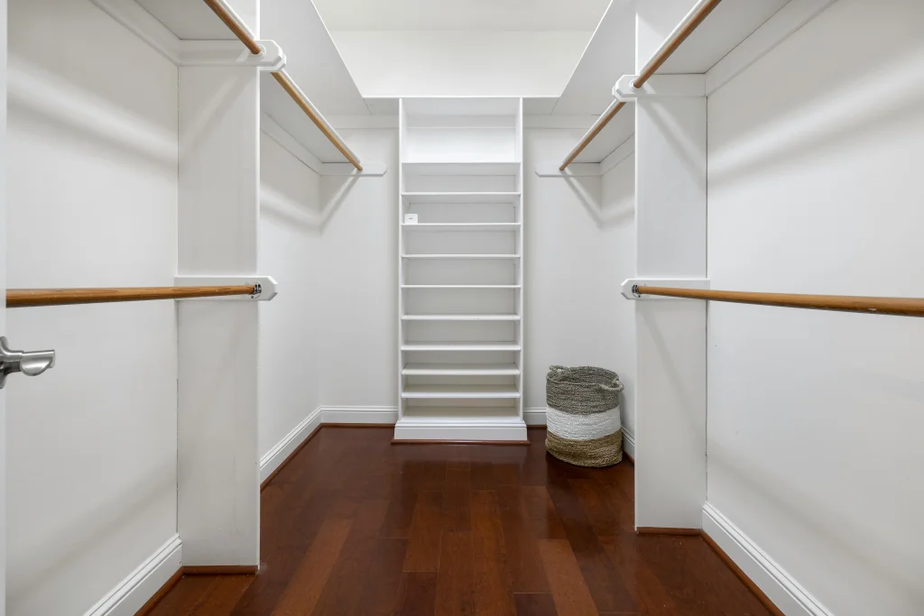 Custom walk-in closet with built-in shoe storage and warm hardwood floor